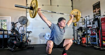 Comment bien faire des squats ? Homme qui fait des squats avec barre de traction dans une salle de sport