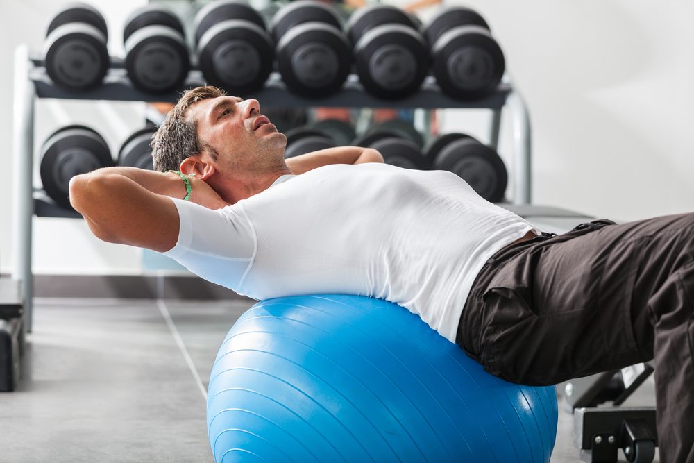 Homme qui réalise un exercice hypopressif sur une balle de sport