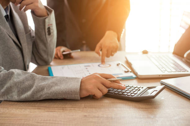 Homme qui se sert d'une calculatrice tandis qu'un autre pointe un document professionnel du doigt