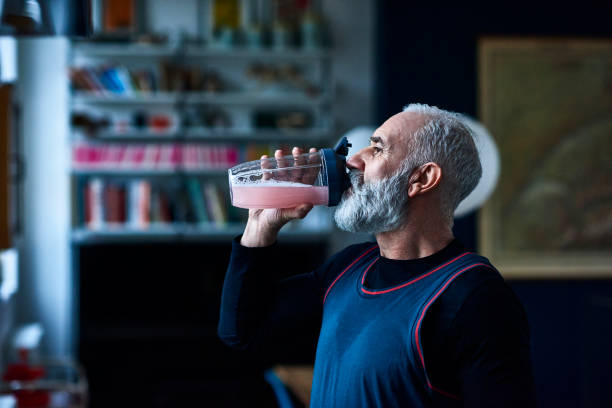 Homme de cinquante ans, de profil, qui boit une boisson énergisante dans un grand verre