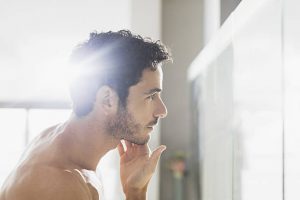 Homme en train d'appliquer un soin sur sa barbe devant le miroir de sa salle de bain