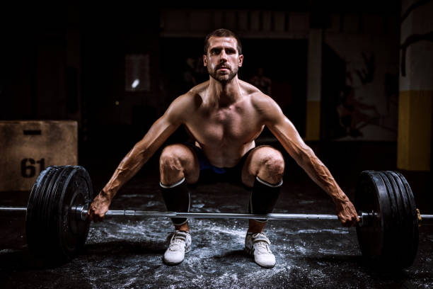 Homme torse-nu qui fait des squats avec une barre chargée de poids