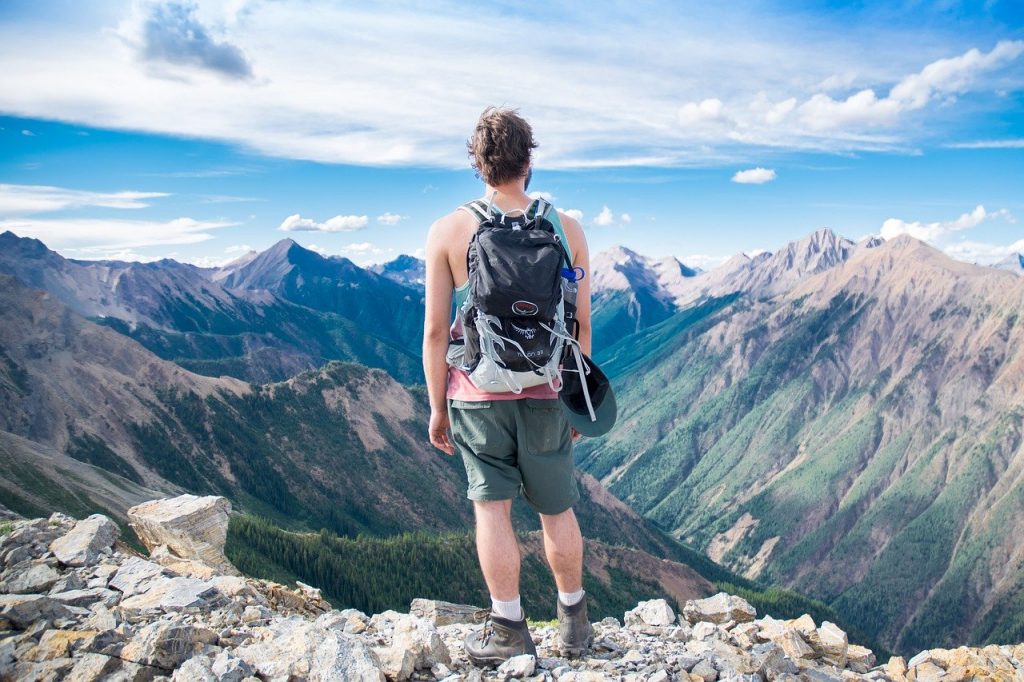 jeune homme avec un sac à dos devant un paysage montagnard